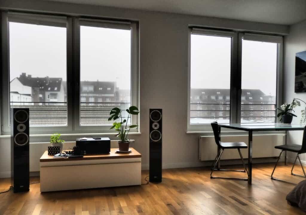 Modern living room with wireless smart speaker on wooden shelf near plants and comfortable sofa